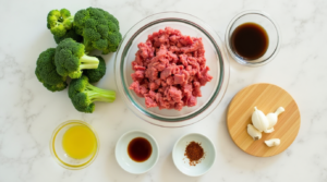 Fresh ingredients for ground beef and broccoli stir-fry, including raw beef, broccoli, soy sauce, garlic, and ginger, neatly arranged on a wooden board.