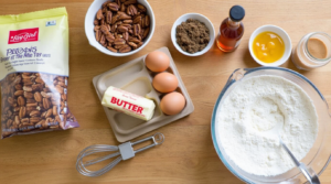 A flat lay of ingredients including pecans, butter, brown sugar, eggs, vanilla, and flour for making Lazy Girl Pecan Pie Bars.