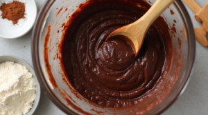 Dark chocolate brownie batter being mixed in a bowl with a wooden spoon."