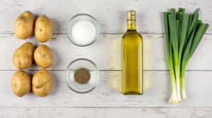 Fresh Russet potatoes, olive oil, salt, black pepper, and green onions on a wooden table.