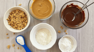 The key ingredients for Butterfinger Balls laid out on a table: Butterfinger, peanut butter, powdered sugar, and melted chocolate.