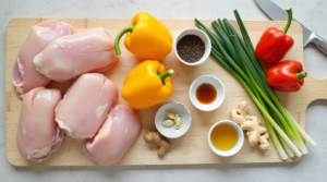 Essential ingredients for Black Pepper Chicken, including chicken, black pepper, soy sauce, garlic, ginger, and fresh vegetables on a wooden cutting board