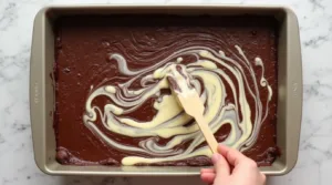 Keto Cheesecake Brownies Brownie and cheesecake batter being swirled together in a baking pan